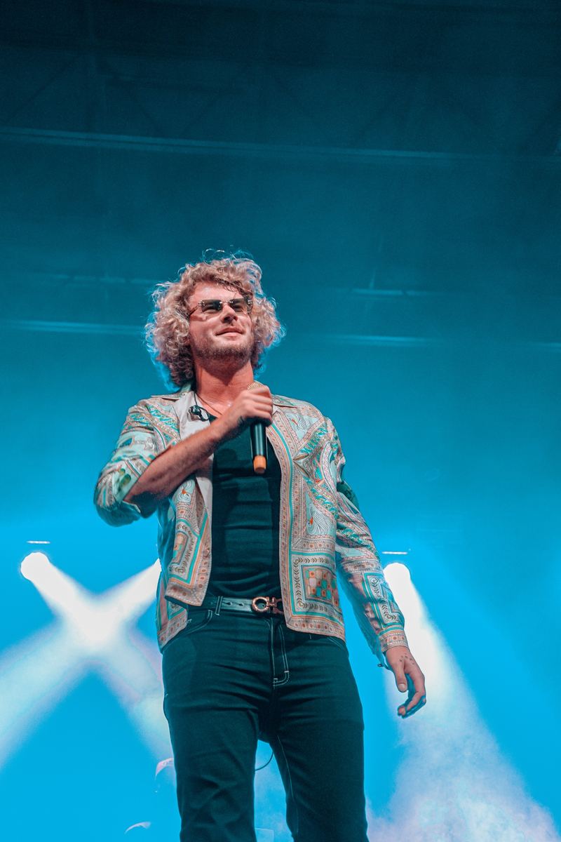 Singer performing under teal stage lighting with crossed light beams